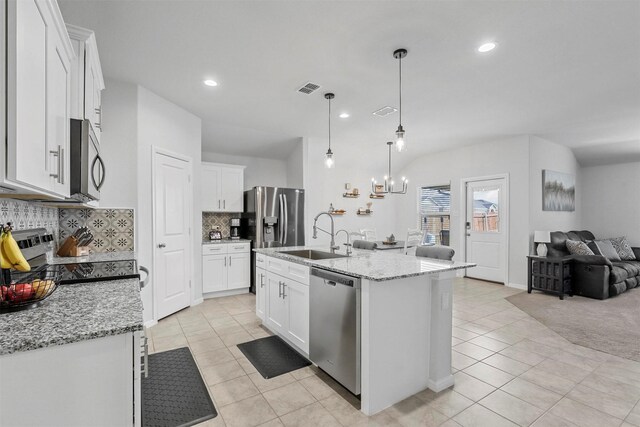 kitchen featuring light stone counters, hanging light fixtures, a center island with sink, stainless steel appliances, and white cabinets