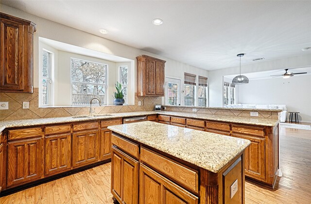 kitchen with sink, hanging light fixtures, tasteful backsplash, light hardwood / wood-style floors, and a kitchen island