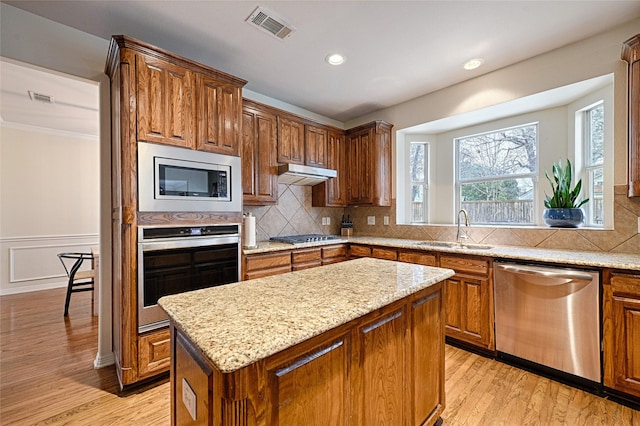 kitchen featuring sink, appliances with stainless steel finishes, a kitchen island, light stone countertops, and light hardwood / wood-style floors