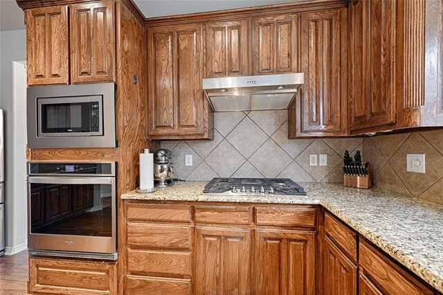 kitchen with sink, a kitchen island, stainless steel appliances, light stone countertops, and light hardwood / wood-style floors