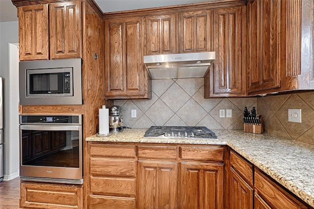 kitchen featuring light stone counters, appliances with stainless steel finishes, decorative backsplash, and hardwood / wood-style flooring