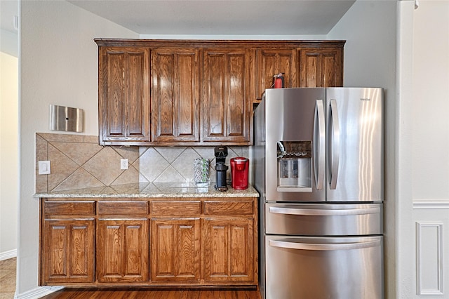 kitchen with light stone countertops, backsplash, and stainless steel fridge with ice dispenser