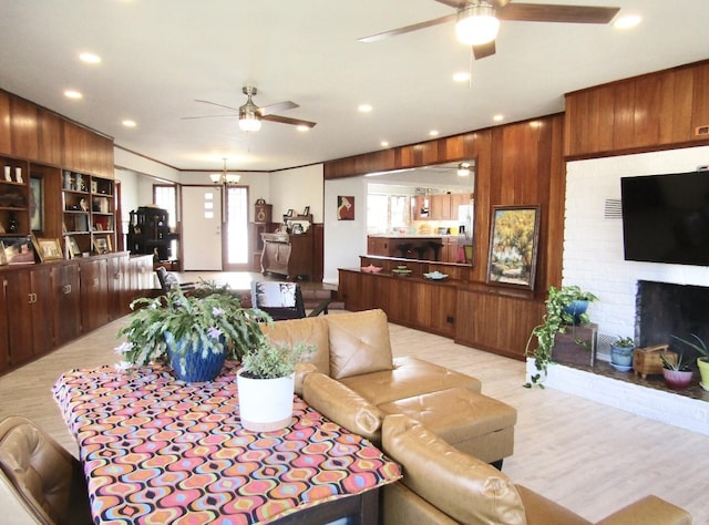 living room with a brick fireplace, ceiling fan with notable chandelier, light hardwood / wood-style floors, and wood walls