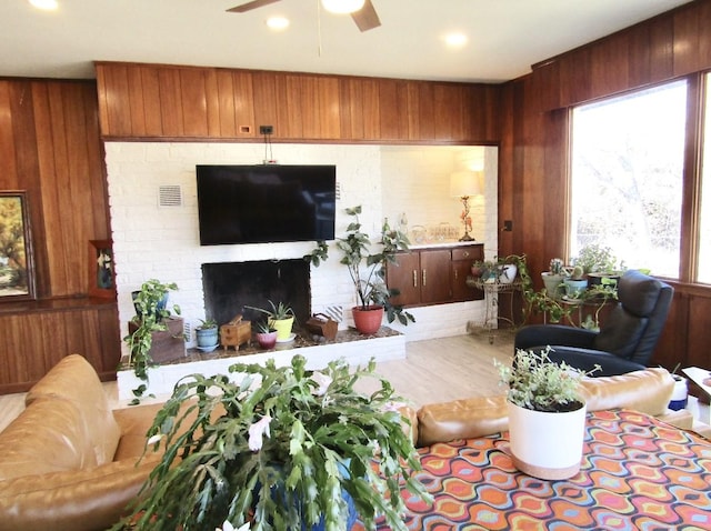 living room with ceiling fan, a brick fireplace, wood-type flooring, and wooden walls