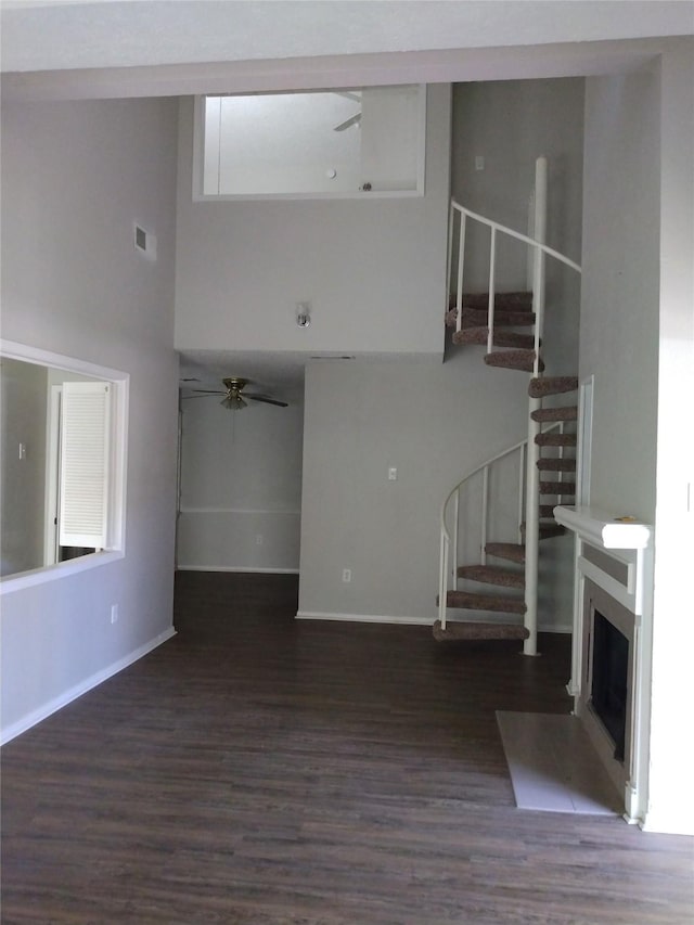 unfurnished living room with ceiling fan, dark hardwood / wood-style floors, and a high ceiling