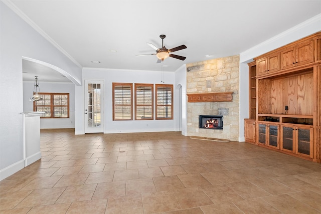 unfurnished living room featuring built in shelves, a stone fireplace, light tile patterned floors, ornamental molding, and ceiling fan