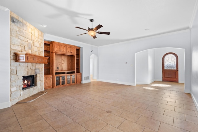 unfurnished living room featuring ceiling fan, ornamental molding, a stone fireplace, and light tile patterned floors