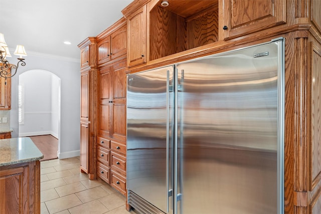 kitchen with light tile patterned floors, crown molding, hanging light fixtures, stainless steel built in refrigerator, and light stone counters