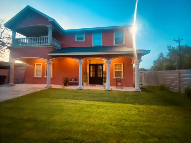 rear view of property featuring a lawn, french doors, and a balcony