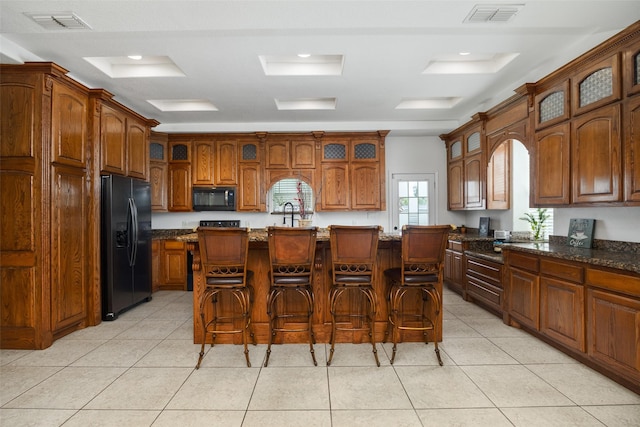 kitchen featuring light tile patterned flooring, a kitchen island with sink, a breakfast bar area, and black appliances