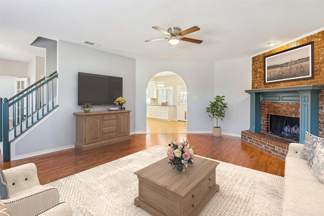 living room featuring ceiling fan, dark hardwood / wood-style flooring, and a brick fireplace