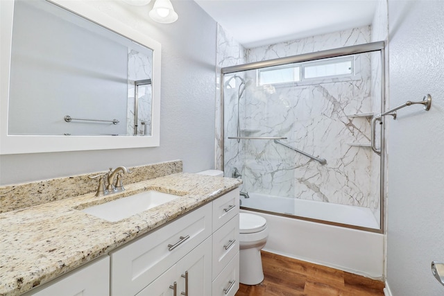 full bathroom with hardwood / wood-style flooring, bath / shower combo with glass door, vanity, and toilet