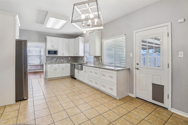 kitchen featuring light tile patterned flooring, appliances with stainless steel finishes, decorative light fixtures, tasteful backsplash, and white cabinetry