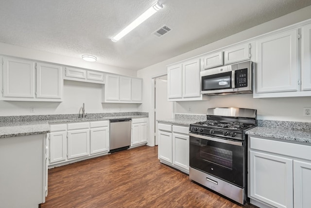 kitchen with dark hardwood / wood-style flooring, light stone counters, stainless steel appliances, and white cabinets