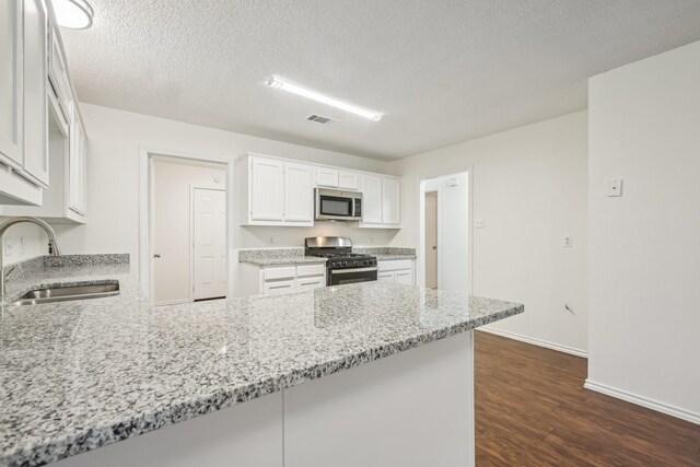 kitchen with sink, white cabinetry, light stone counters, range with gas cooktop, and kitchen peninsula