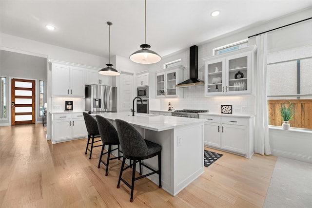 kitchen featuring sink, white cabinetry, a center island with sink, stainless steel appliances, and wall chimney range hood