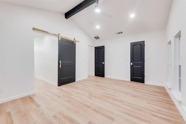 empty room featuring a barn door, vaulted ceiling with beams, ceiling fan, and light hardwood / wood-style flooring