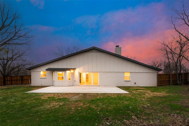 back house at dusk featuring a lawn and a patio