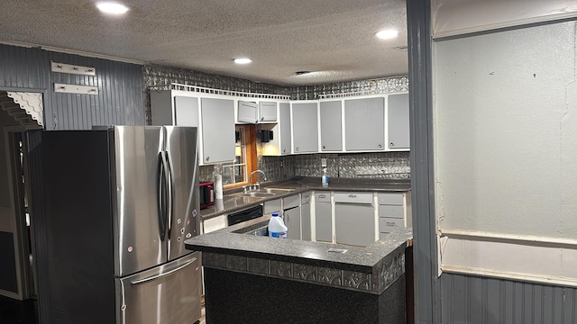 kitchen with dark countertops, freestanding refrigerator, a sink, and a textured ceiling