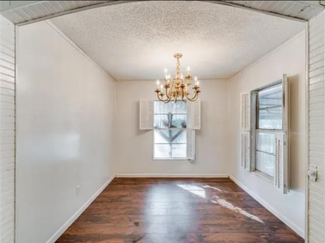 unfurnished dining area with a notable chandelier, a textured ceiling, baseboards, and dark wood-style flooring