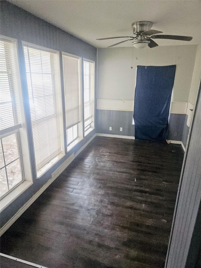 spare room featuring ceiling fan, dark wood-style flooring, wainscoting, and baseboards