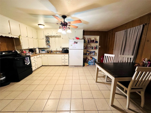 kitchen with light tile patterned floors, wooden walls, white refrigerator, white cabinets, and black range with electric cooktop