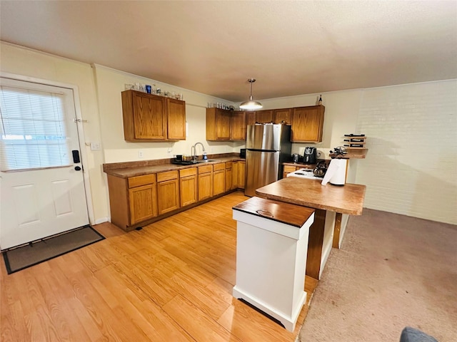 kitchen with hanging light fixtures, sink, stainless steel refrigerator, and light wood-type flooring