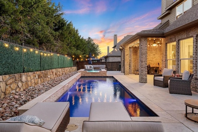 pool at dusk with an outdoor living space, a patio, pool water feature, and an in ground hot tub