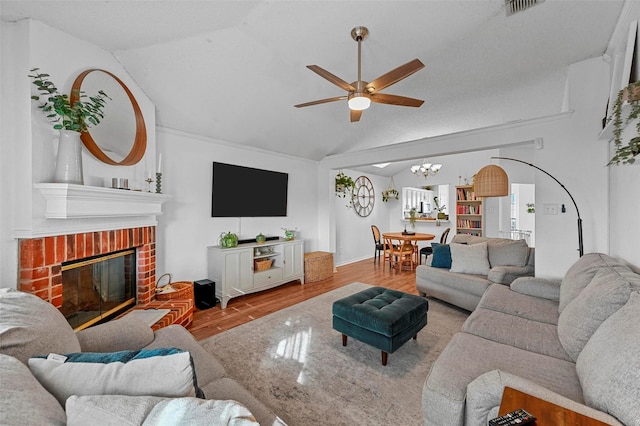 living room with ceiling fan with notable chandelier, a fireplace, vaulted ceiling, and light wood-type flooring