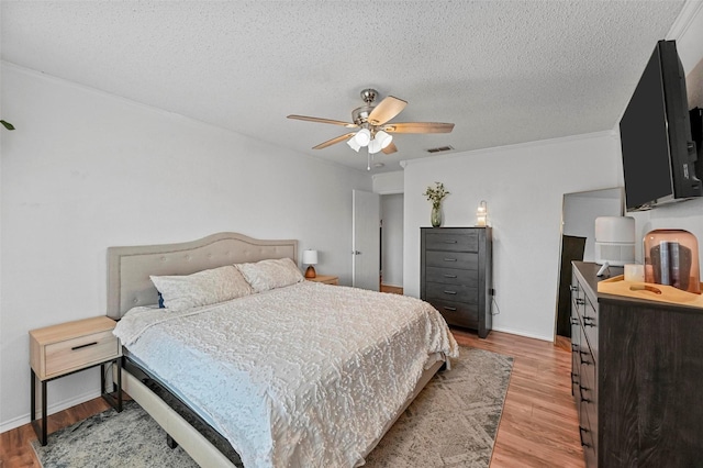 bedroom featuring crown molding, a textured ceiling, light hardwood / wood-style floors, and ceiling fan