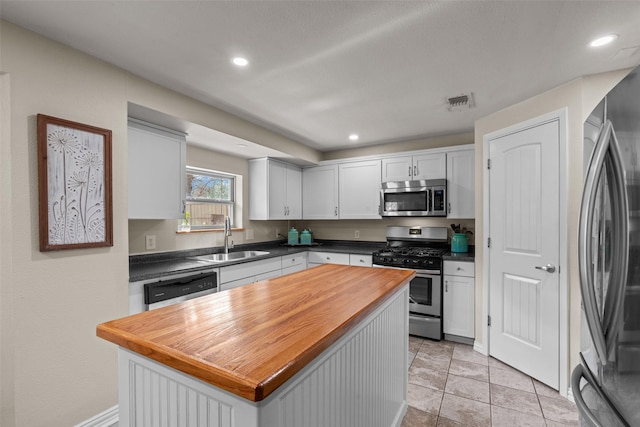 kitchen with sink, stainless steel appliances, a center island, white cabinets, and wood counters