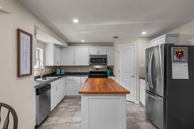 kitchen with appliances with stainless steel finishes, sink, wooden counters, white cabinets, and a center island