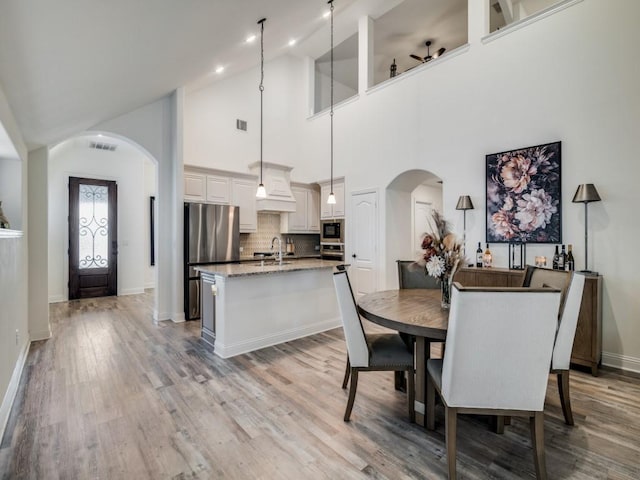 dining area featuring sink, light wood-type flooring, and a high ceiling