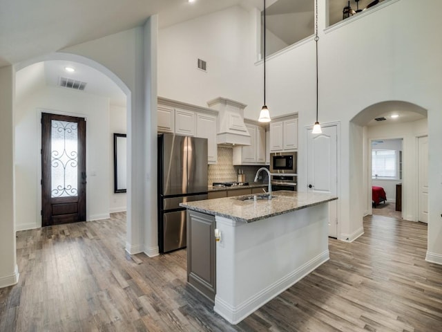 kitchen with appliances with stainless steel finishes, light stone counters, a center island with sink, decorative backsplash, and decorative light fixtures