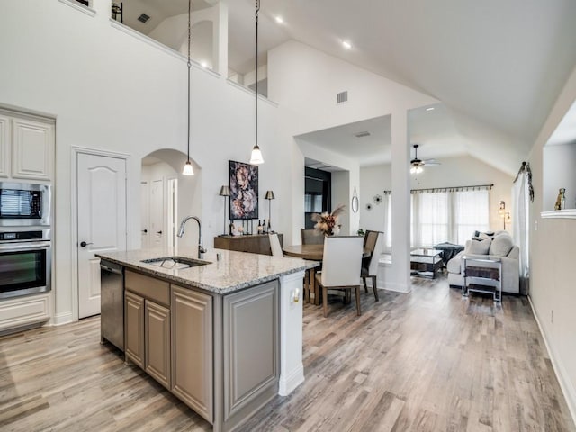 kitchen with sink, appliances with stainless steel finishes, an island with sink, pendant lighting, and light stone countertops