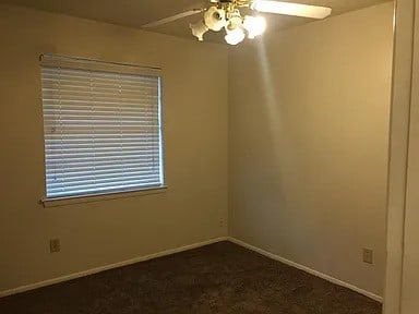 unfurnished room featuring ceiling fan and dark colored carpet