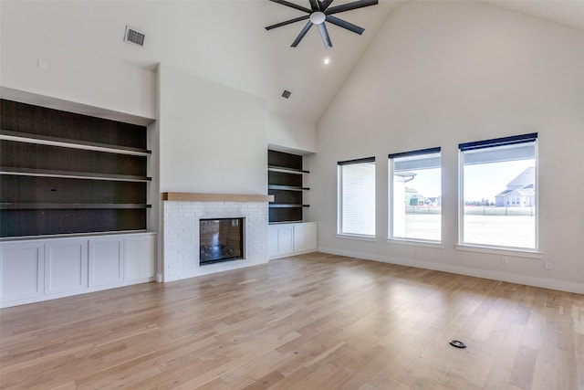 unfurnished living room featuring ceiling fan, a brick fireplace, built in features, and light wood-type flooring