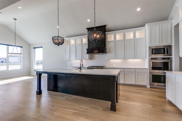 kitchen with white cabinetry, appliances with stainless steel finishes, a kitchen island with sink, and hanging light fixtures