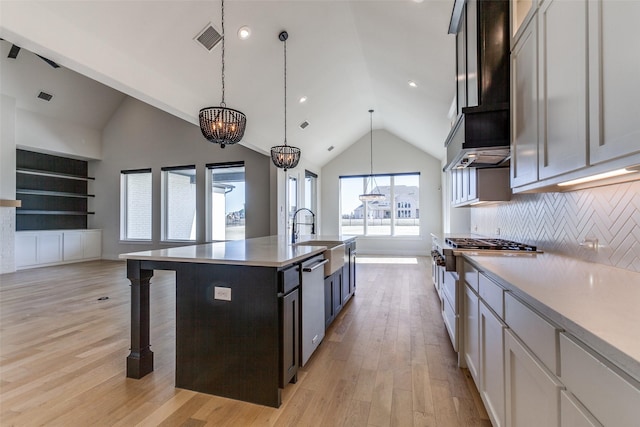 kitchen featuring pendant lighting, tasteful backsplash, an island with sink, stainless steel appliances, and light wood-type flooring