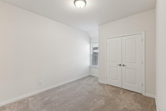 unfurnished bedroom featuring vaulted ceiling, light carpet, and a closet