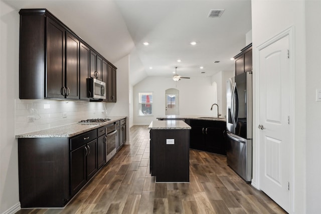 kitchen with sink, tasteful backsplash, light stone counters, a center island with sink, and appliances with stainless steel finishes