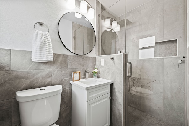 bathroom featuring a shower with door, vanity, tile walls, and toilet