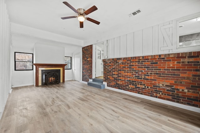 unfurnished living room featuring ceiling fan, brick wall, and light wood-type flooring