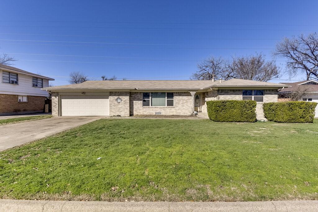 single story home featuring an attached garage, concrete driveway, brick siding, and a front yard