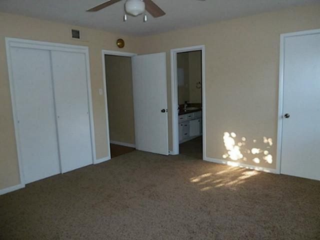 unfurnished bedroom with dark carpet, ensuite bath, and ceiling fan