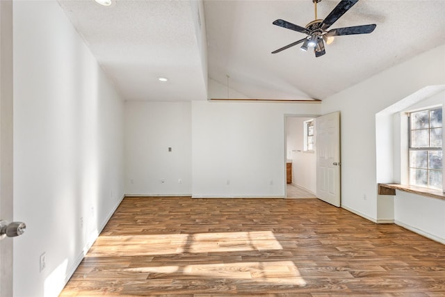 spare room featuring ceiling fan, vaulted ceiling, light hardwood / wood-style flooring, and a textured ceiling