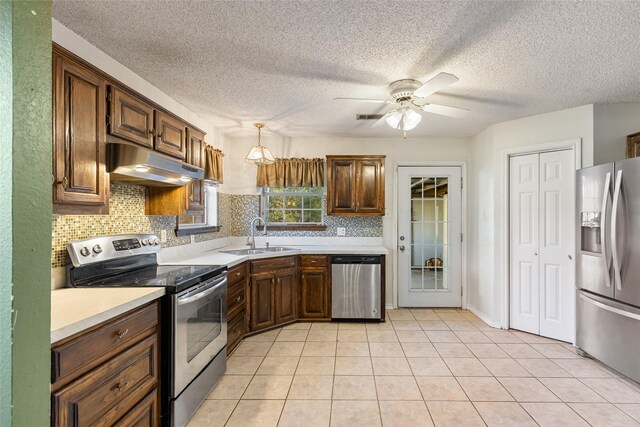 kitchen featuring appliances with stainless steel finishes, sink, backsplash, hanging light fixtures, and light tile patterned floors