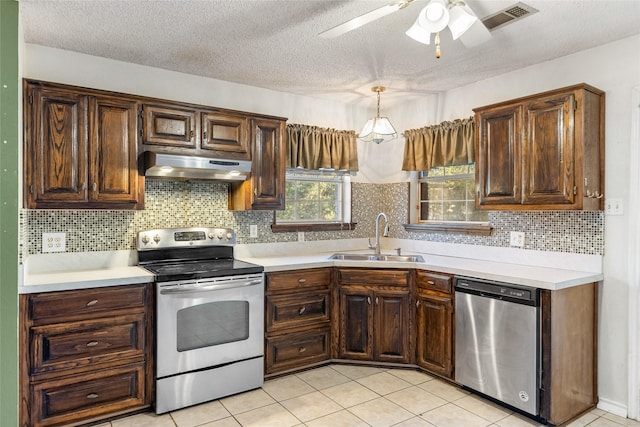 kitchen with appliances with stainless steel finishes, sink, hanging light fixtures, light tile patterned floors, and a textured ceiling