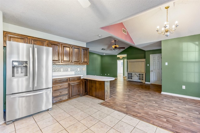 kitchen with vaulted ceiling, stainless steel fridge with ice dispenser, decorative light fixtures, decorative backsplash, and kitchen peninsula