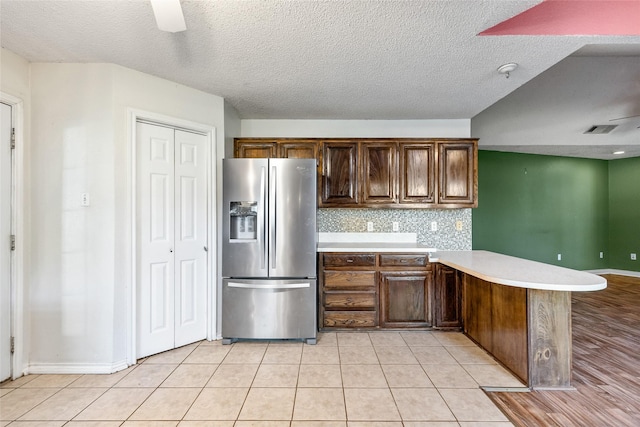 kitchen with stainless steel fridge with ice dispenser, a textured ceiling, light tile patterned floors, kitchen peninsula, and decorative backsplash